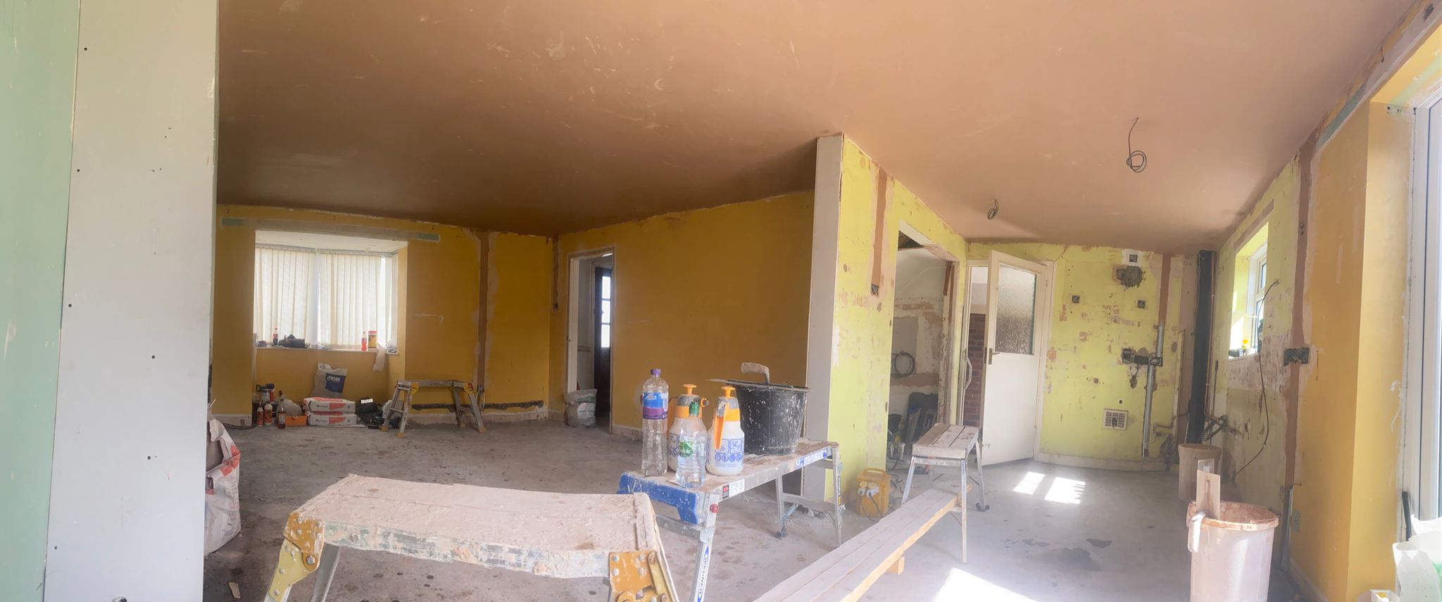 Panorama of an open-plan room mid-job, with a freshly plastered ceiling and work benches