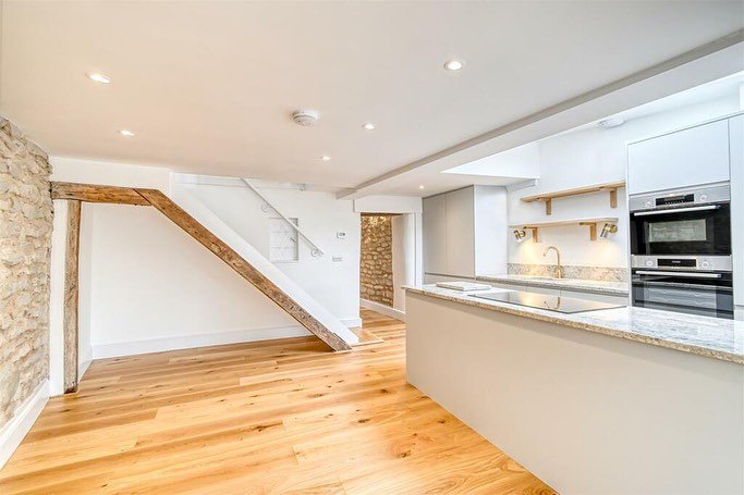 An open kitchen with smooth plastered walls and an oak staircase