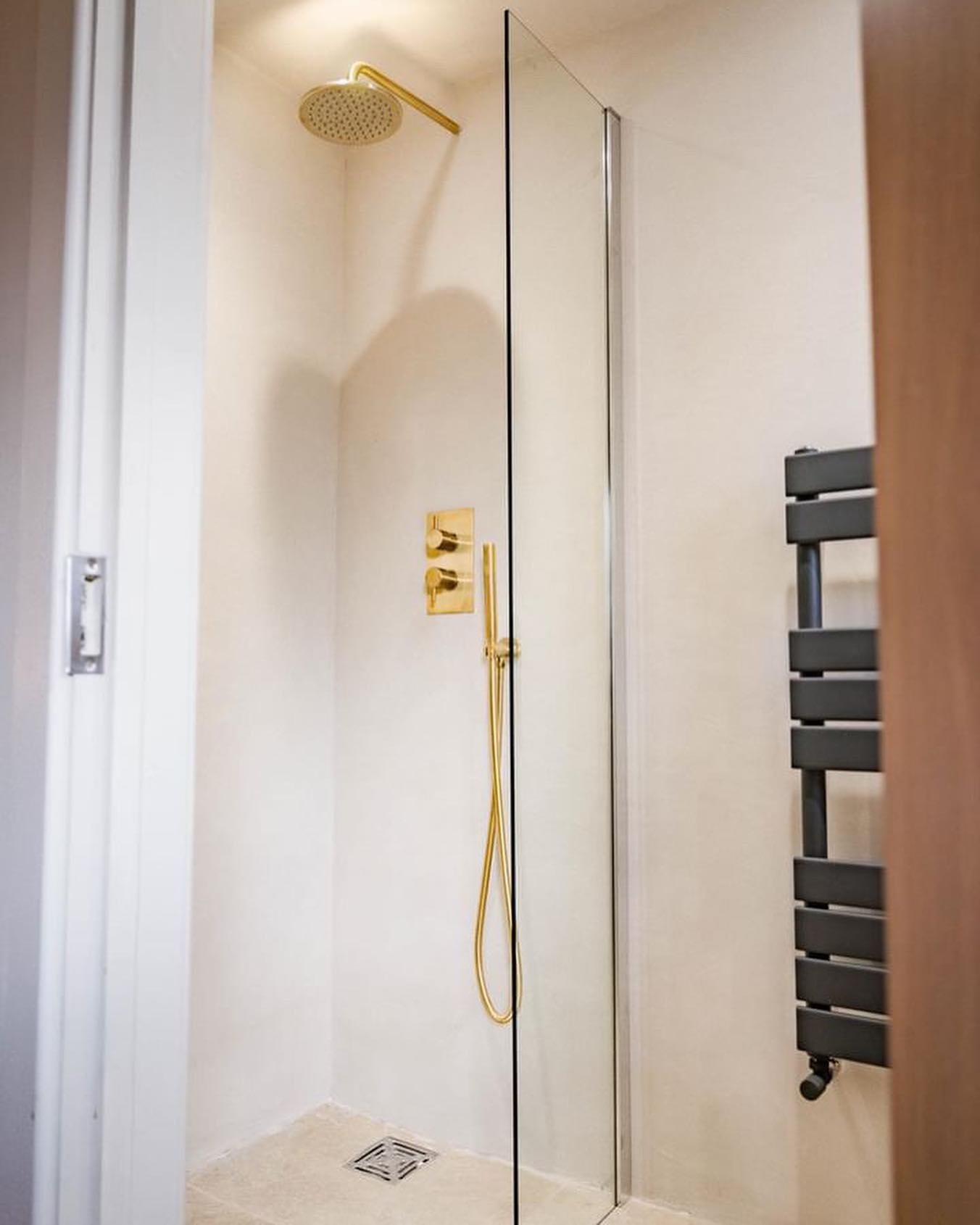 A walk-in shower finished in pale polished tadelakt with brushed brass fittings