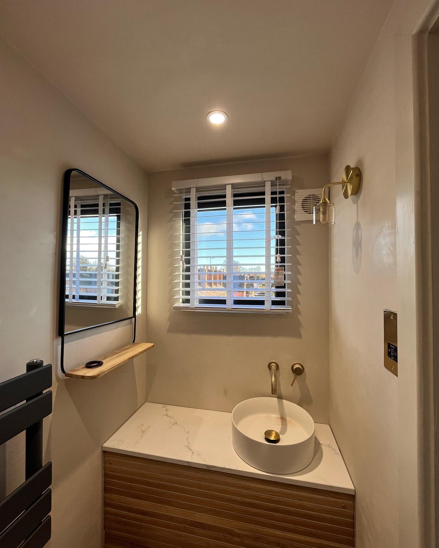 A small tadelakt en-suite with a black mirror and brass wall lights