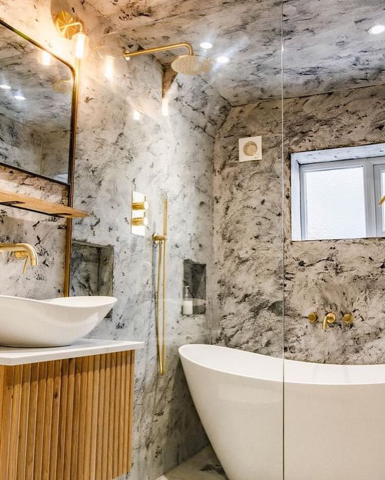 A finished two-tone tadelakt bathroom with a freestanding bath, fluted oak vanity and brass fittings