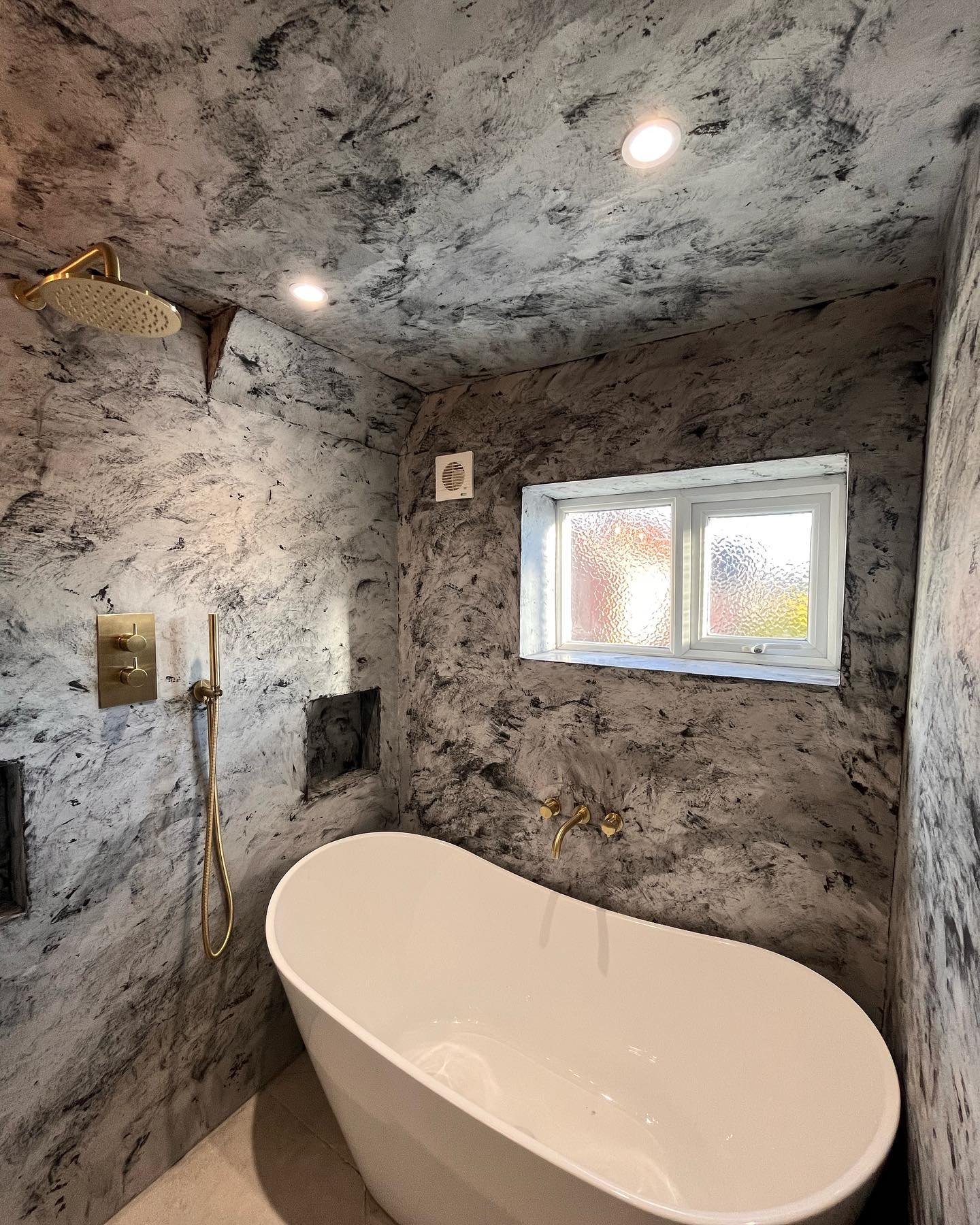 Two-tone tadelakt bathroom with a freestanding bath beneath the window