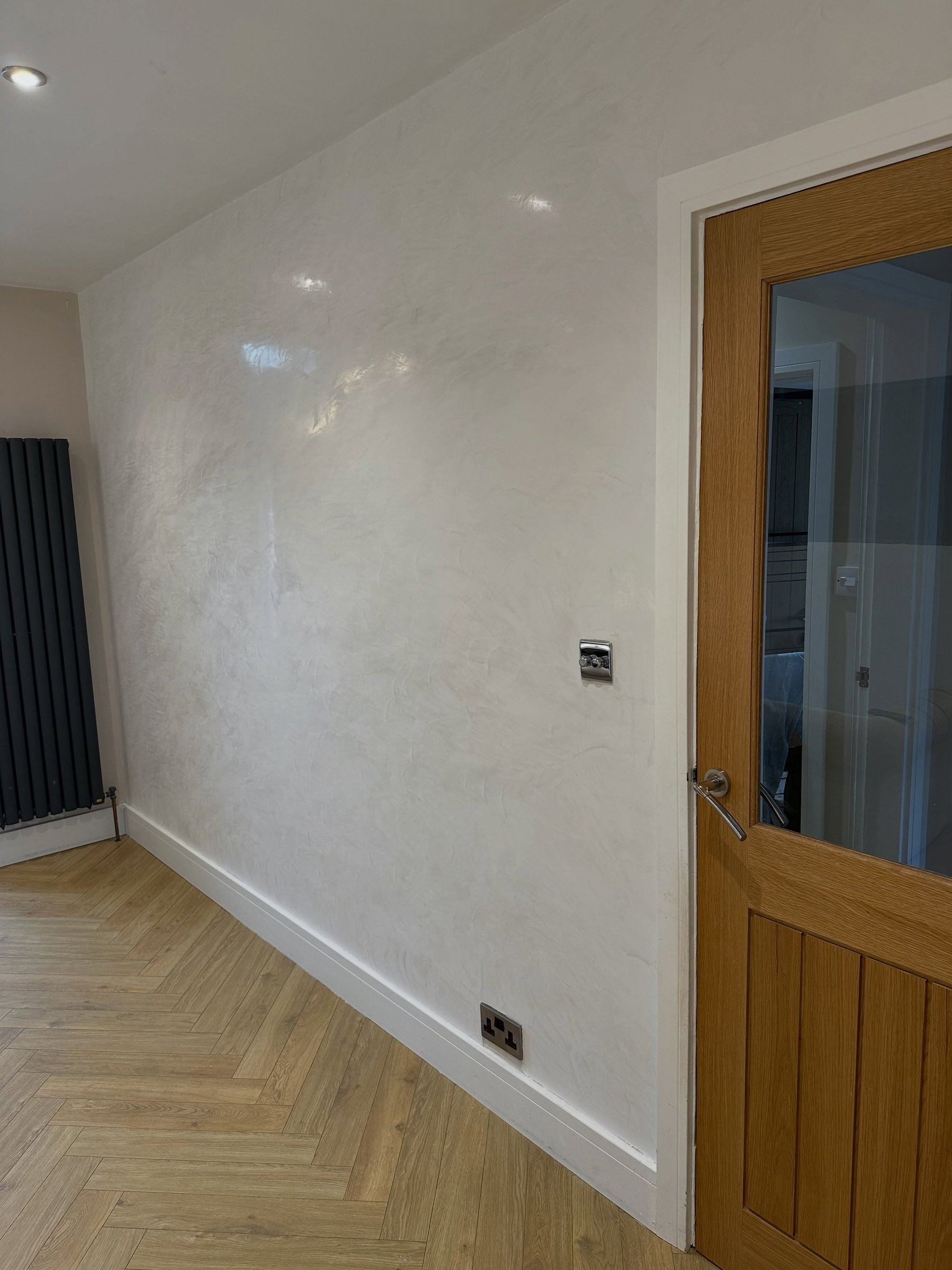 An off-white polished Venetian plaster feature wall in a hallway with an oak door